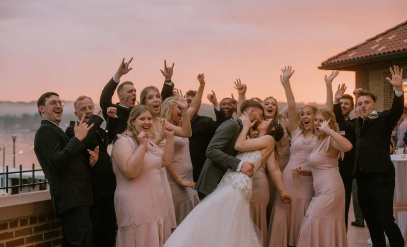 Bride and groom kiss as wedding party cheers them on at sunset- image by Anna Gutermuth Photography