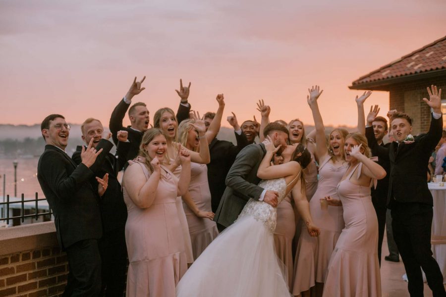 Bride and groom kiss as wedding party cheers them on at sunset- image by Anna Gutermuth Photography