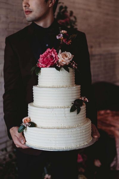 Groom holds 4 tiered cake from The Cupcake Couture in De Pere, WI