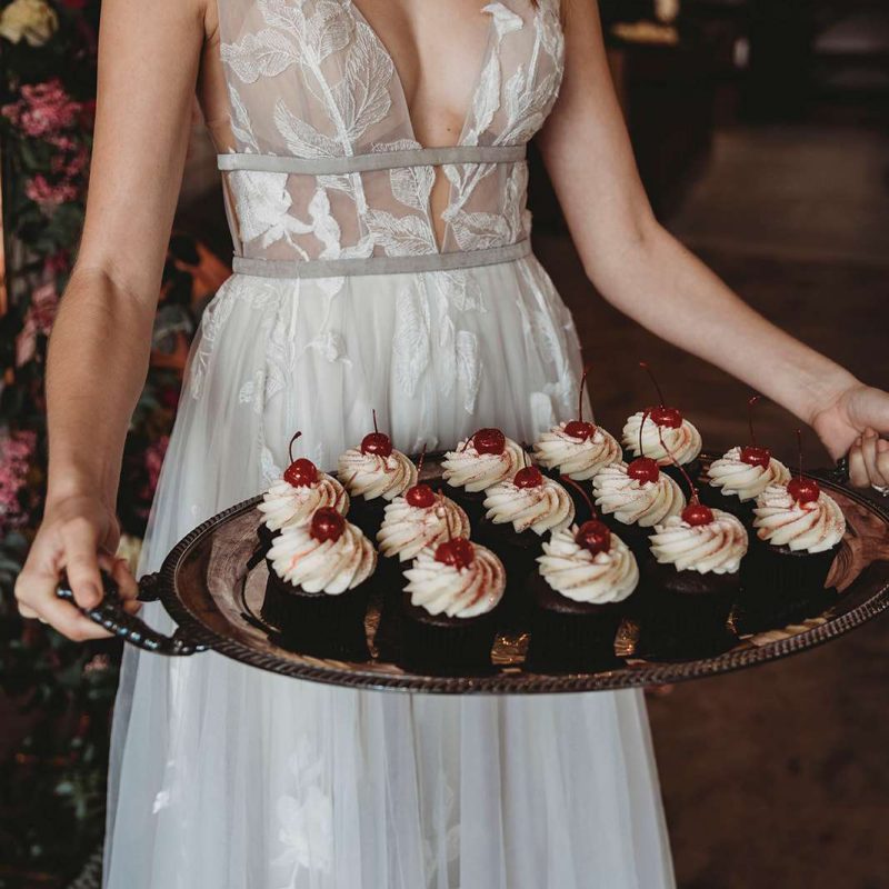 Bride in stunning gown holds a tray of decadent cupcakes from The Cupcake Couture in De Pere.
