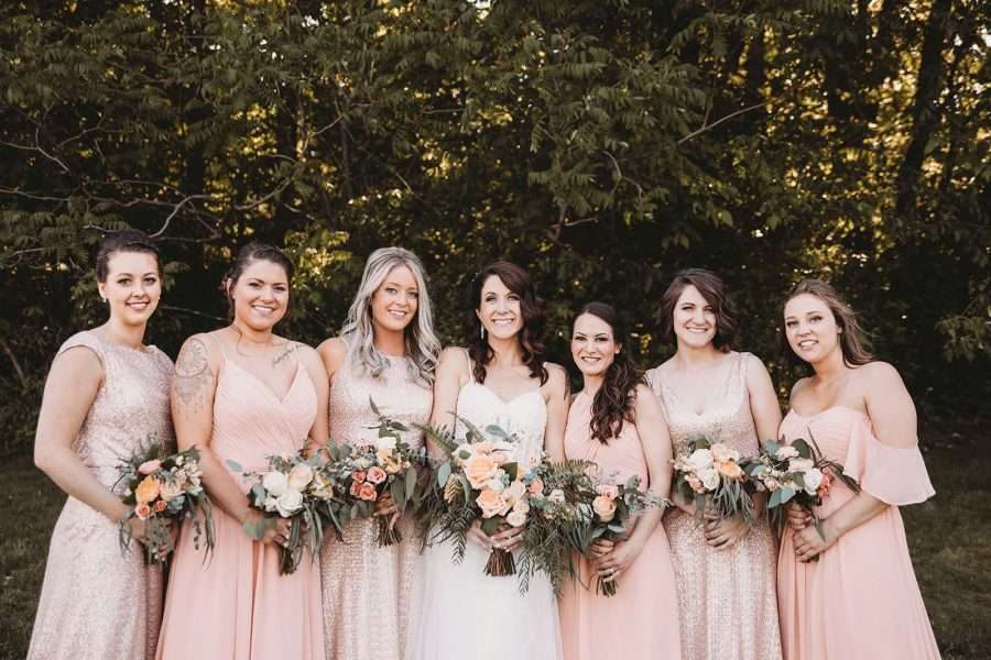 Bridal party poses with their bouquets in soft peach hues.