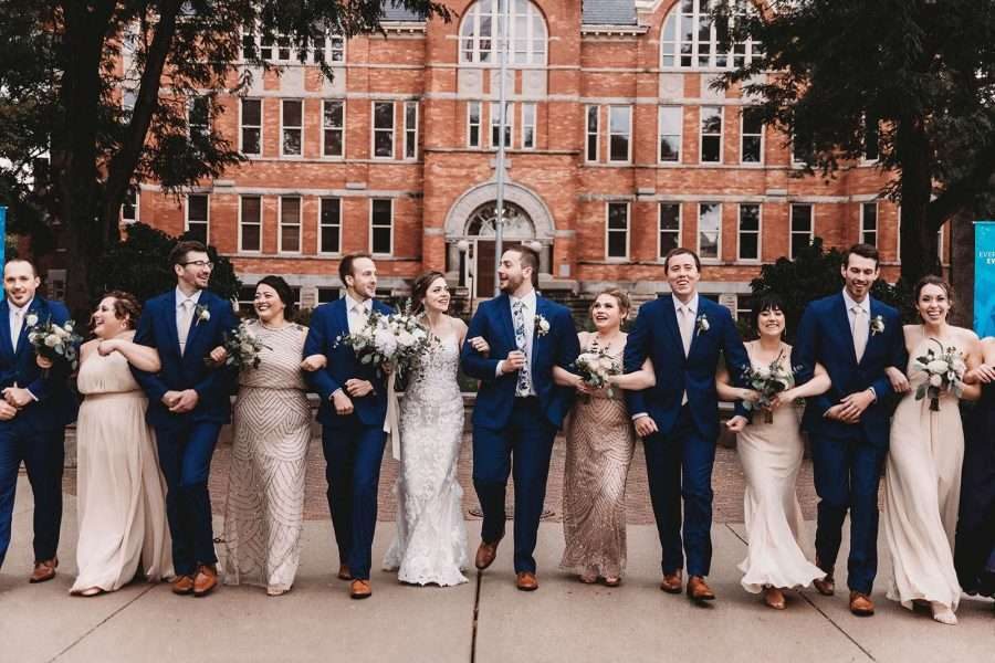 Wedding party walks arm in arm outside of St. Norbert's College in De Pere, WI.