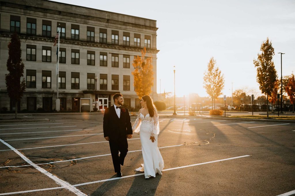 Bride and groom walk hand in hand in golden light in downtown Oshkosh. 