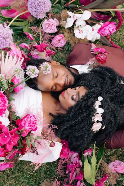 Bride and groom lay amongst bright pink flowers.